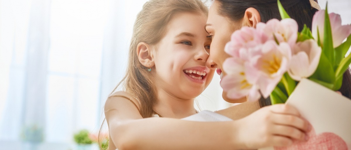 Eine Mädchen überreicht ihrer Mama Blumen und eine Grußkarte