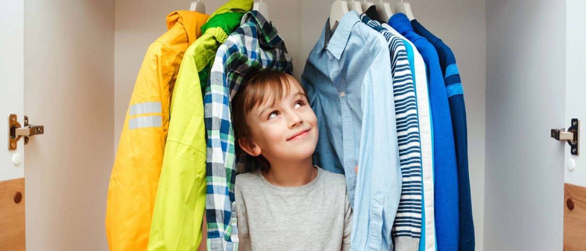 Ein Junge steht in einem Kleiderschrank mit wenig Kleidung