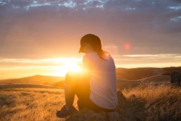 Eine Frau sitzt auf einem Berg im Sonnenuntergang und sucht den Sinn des Lebens